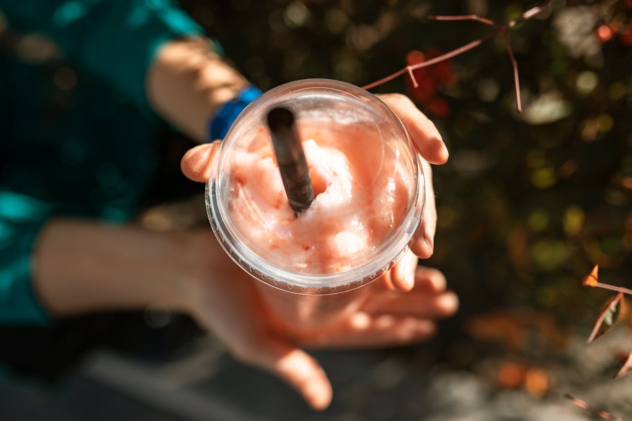 gallery-04 Close-up of a hand holding a refreshing strawberry smoothie in sunlight.